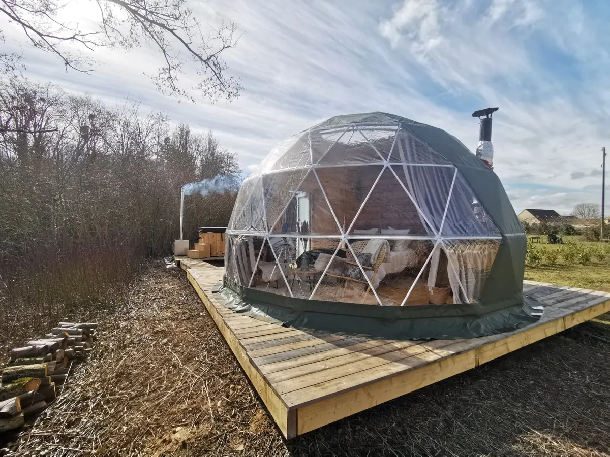 Dôme géodésique terminé sur sa terrasse en bois, fumée du poêle à bois